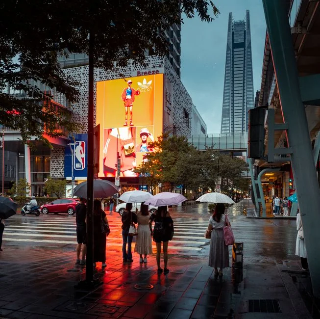 People with umbrellas crossing a wet street in downtown Taipei, with illuminated billboards and skyscrapers in the background. - 3d led billboards in china