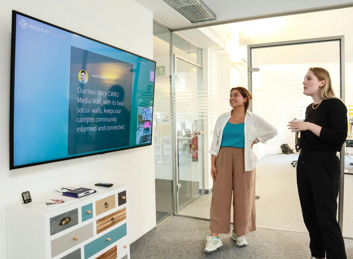Two employees checking the company news on a screen at the office - projection on wall vs screen